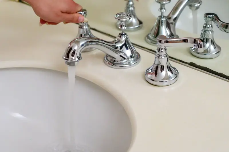 Hand turning the handle of a chrome bathroom faucet with water running