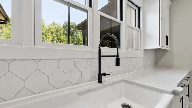 Bright white kitchen with a farmhouse sink and black faucet under large windows