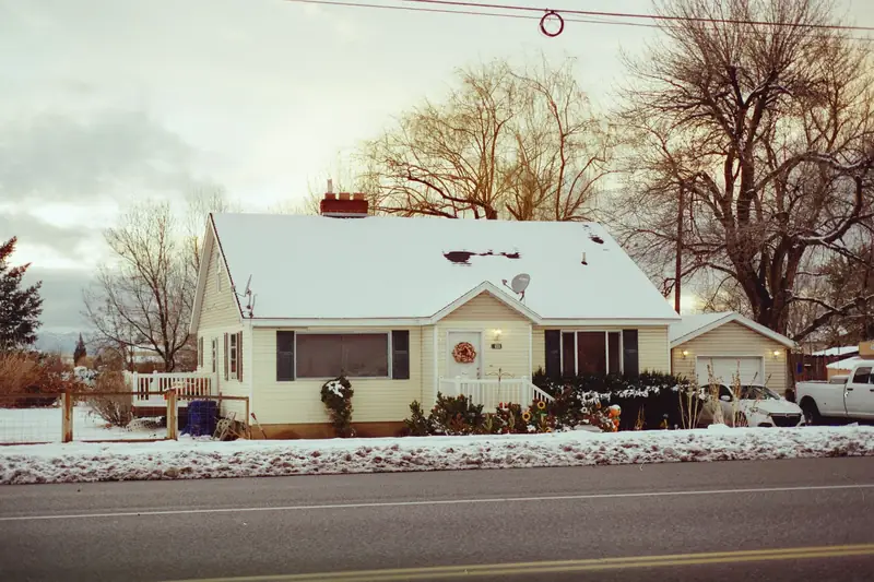 Small house with a snow-covered roof and frosty yard on a winter day